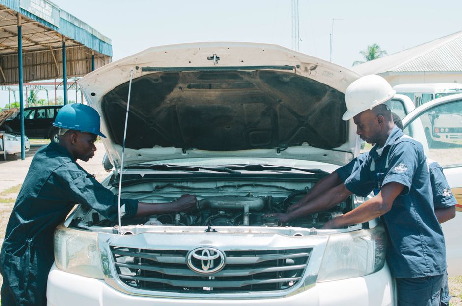 Two auto mechanics in Nigeria working on a car engine outdoors, showcasing teamwork in vehicle repair.